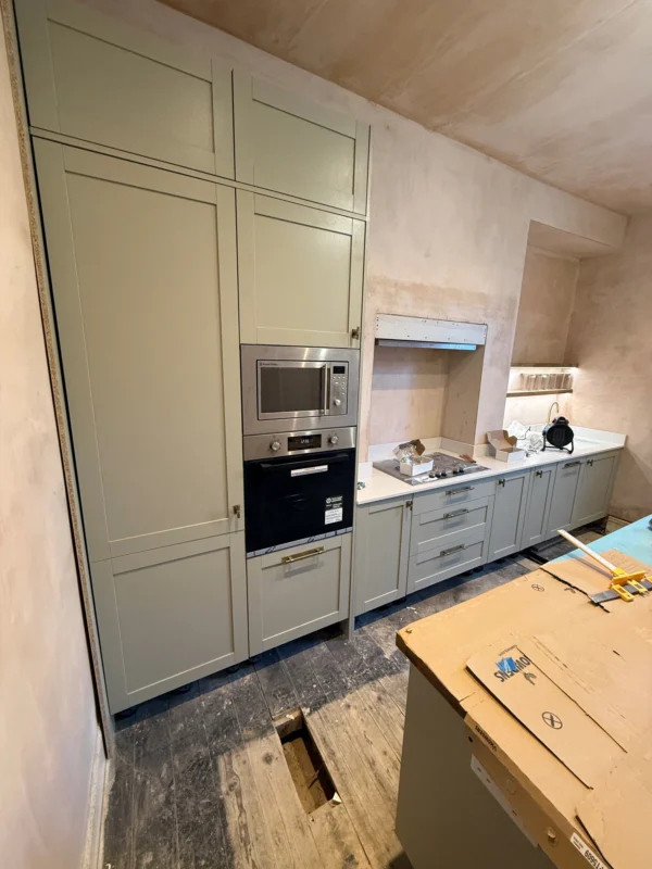 A kitchen under renovation with sage green cabinetry.