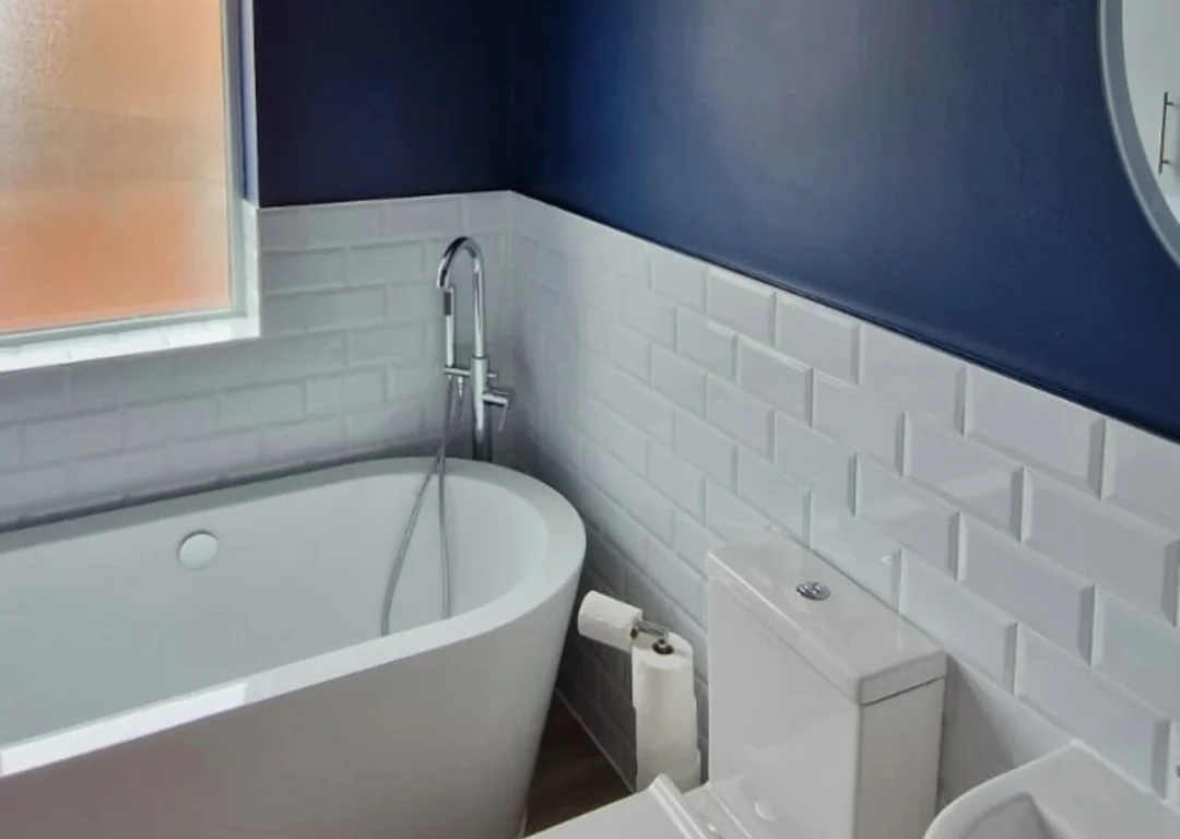 A bathroom with white tiles and dark blue walls.