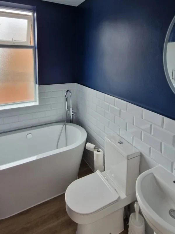 A bathroom with white tiles and dark blue walls.