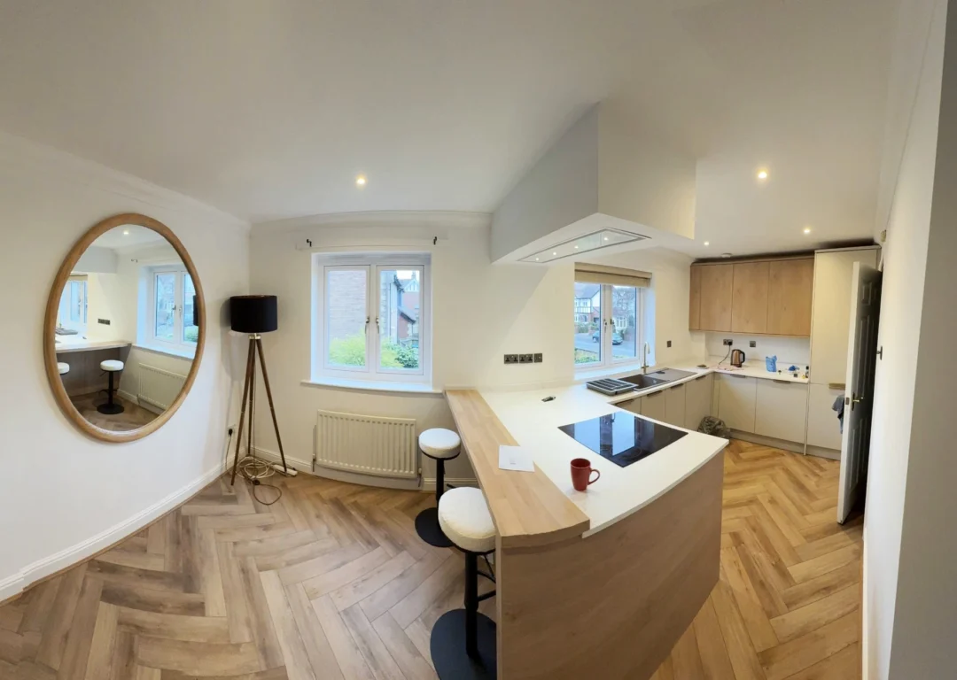 A large kitchen with a bar feature, wood flooring and light colours.