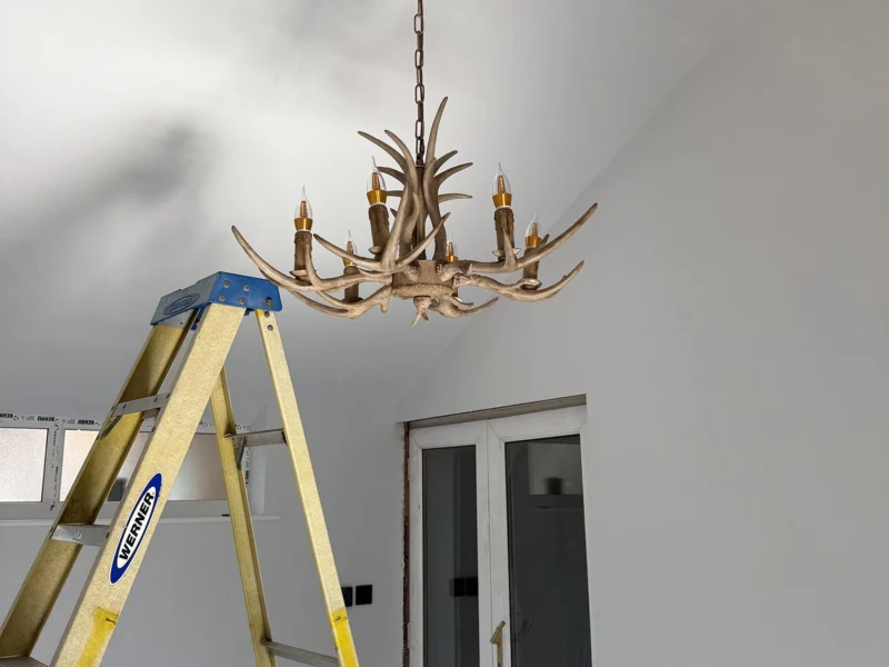 A person uses a ladder to reach the ceiling in a room, indicating maintenance or painting work in progress.