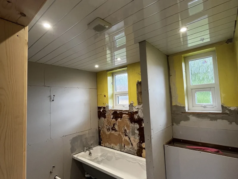 A bathroom under construction featuring a bathtub and toilet, with exposed walls and tools scattered around.