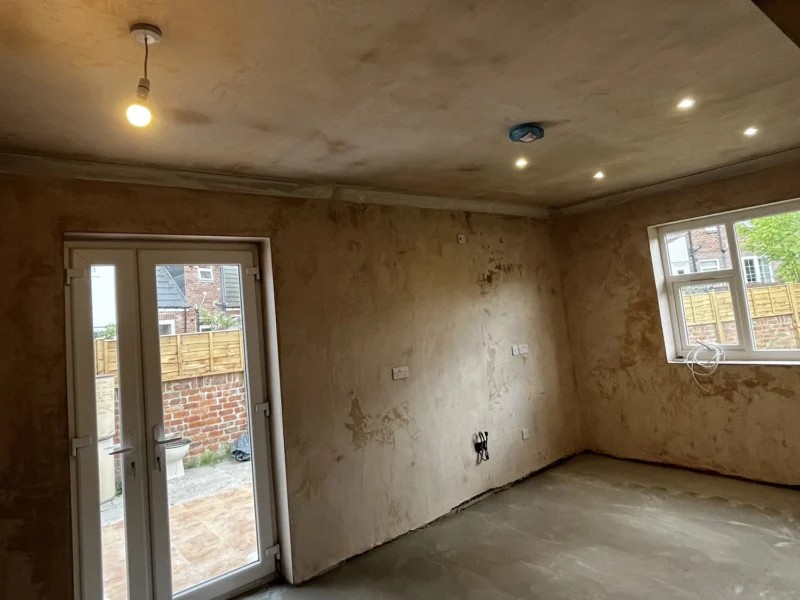 A room mid refurbishment featuring a concrete floor and a single door, creating a minimalist and industrial atmosphere.