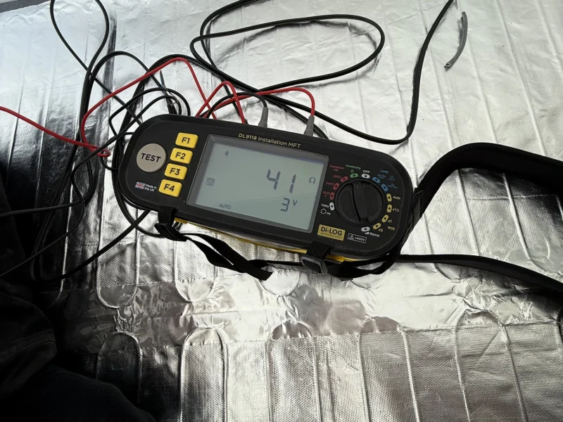 A digital multimeter placed on a reflective piece of foil, displaying various measurement settings and readings.