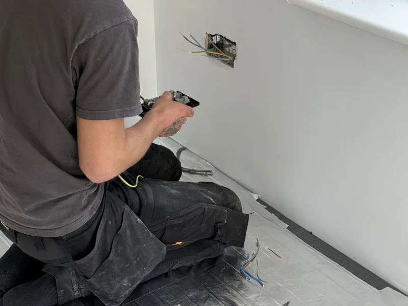 A man sitting on the floor surrounded by wires and tools, focused on a project or repair task.