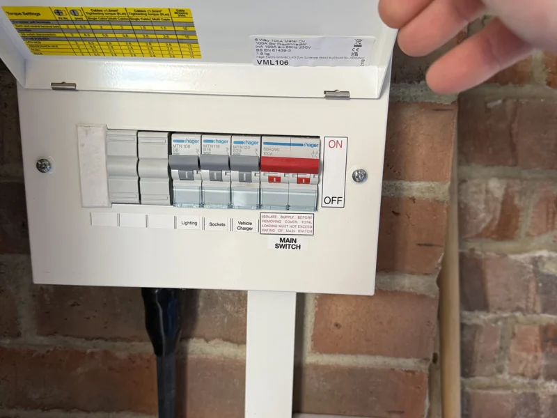 A person is reaching to flip a switch on a fusebox on a wall.